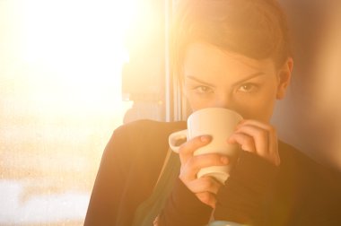 Güneş penceresi üzerinde sıcak kahve ile güzel bir genç kadın