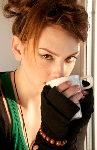 Beautiful young woman with cup of coffee over window — Stock Photo, Image