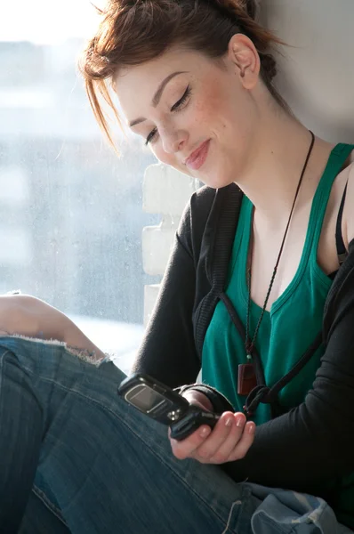 Pencere cep telefonu ile güzel bir genç kadın. — Stockfoto