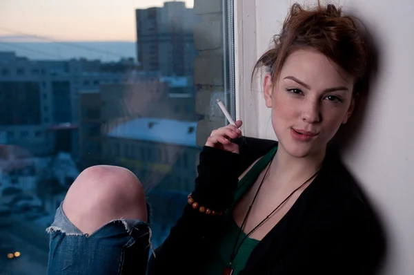 Mooie jonge vrouw roken op avond venster. — Stockfoto