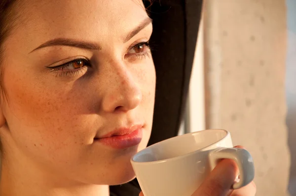 Beautiful young woman with cup of coffee over window — Stock Photo, Image