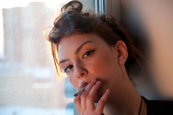 Beautiful young woman smoking on evening window. — Stock Photo, Image