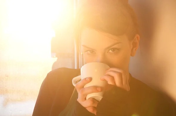 Красивая молодая женщина с чашкой горячего кофе над солнцем окно — стоковое фото