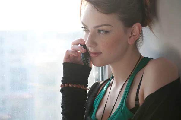 Vacker ung kvinna med mobiltelefon på fönster. — Stockfoto