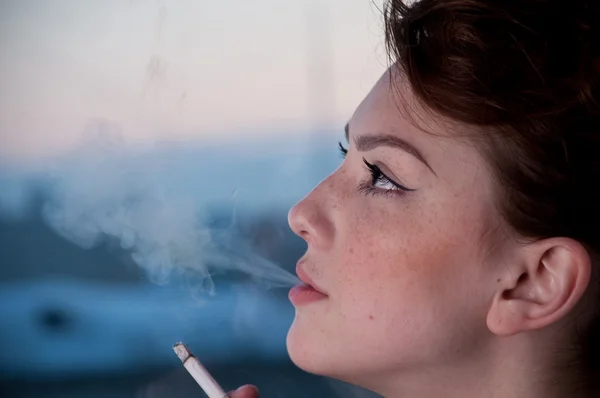 美丽的年轻女子在晚上窗口上吸烟. — 图库照片
