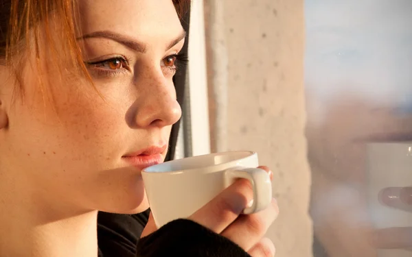 Красивая молодая женщина с чашкой кофе над окном — стоковое фото