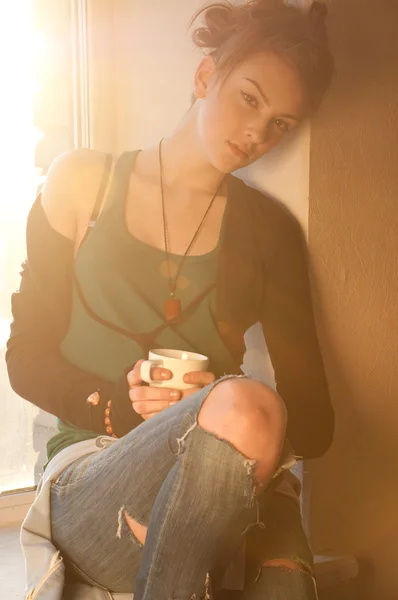 Beautiful young woman with cup of hot coffee over sun window — Stock Photo, Image
