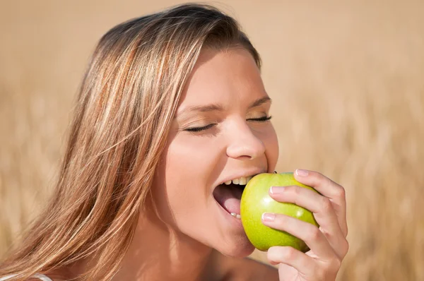 Žena v pšeničné pole jíst zelené jablko. letní piknik. — Stock fotografie