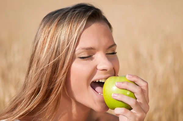 Mulher no campo de trigo a comer maçã verde. Piquenique de verão . — Fotografia de Stock