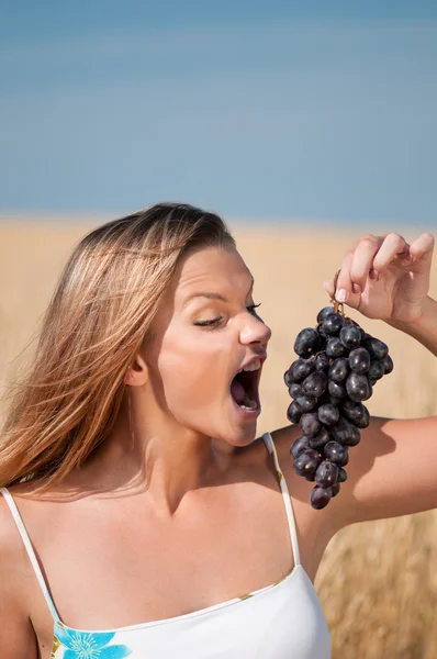 麦畑のブドウを食べるの女性。夏のピクニック. — ストック写真