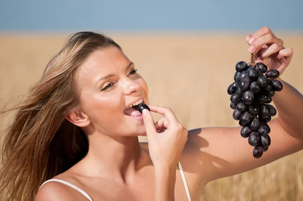 Donna nel campo di grano che mangia uva. Picnic estivo . — Foto Stock