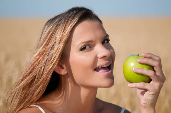 Woman in wheat field eating green apple. Summer picnic. — Stock Photo, Image