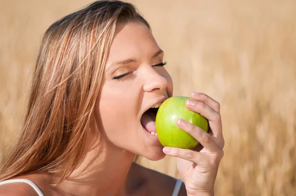 Mulher no campo de trigo a comer maçã verde. Piquenique de verão . — Fotografia de Stock