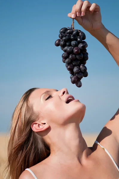 Woman in wheat field eating grapes. Summer picnic. — Stock Photo, Image