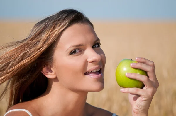 Woman in wheat field eating green apple. Summer picnic. — Stock Photo, Image