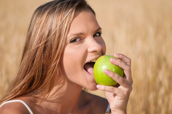 Donna nel campo di grano che mangia mela verde. Picnic estivo . — Foto Stock