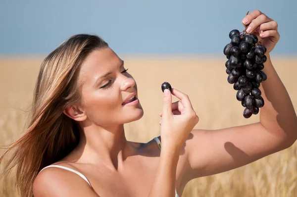 stock image Woman in wheat field eating grapes. Summer picnic.