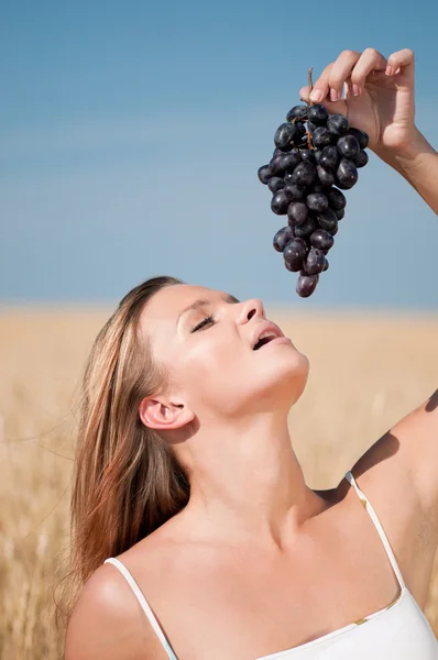 Жінка в пшеничному полі їсть виноград. Літній пікнік . — стокове фото