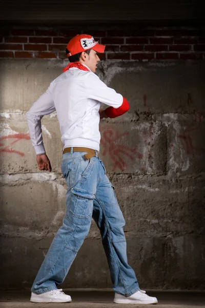 灰色のレンガの壁の上にモダンなスタイルで踊るヒップホップの少年 — ストック写真
