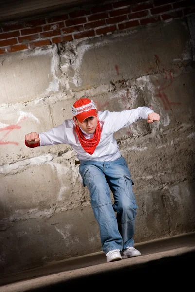 灰色のレンガの壁の上にモダンなスタイルで踊るヒップホップの少年 — ストック写真