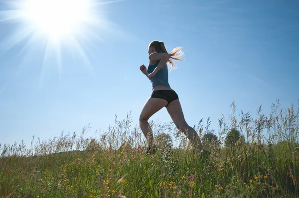 Спортивная женщина бегает по зеленой траве и небу — стоковое фото