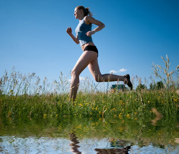 Sport kvinna kör över grönt gräs och sky — Stockfoto