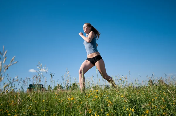 Sportovní žena běží přes zelené trávy a obloha — Stock fotografie