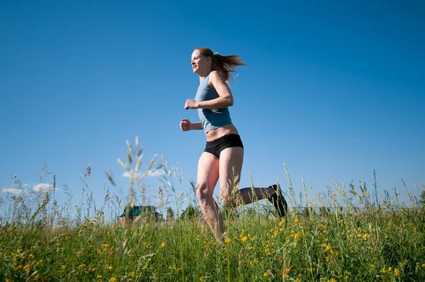 Sport woman running over green grass and sky — Stock Photo, Image