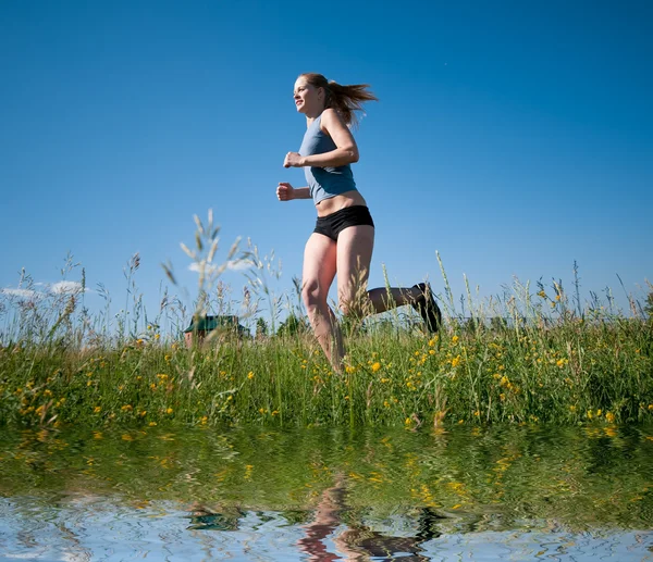 Sport kvinna kör över grönt gräs och sky — Stockfoto