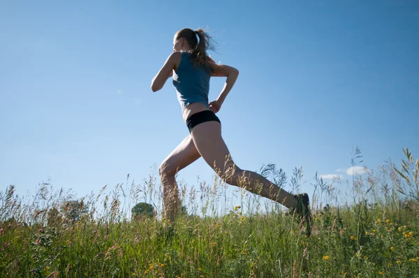 Спортивна жінка біжить над зеленою травою і небом — стокове фото