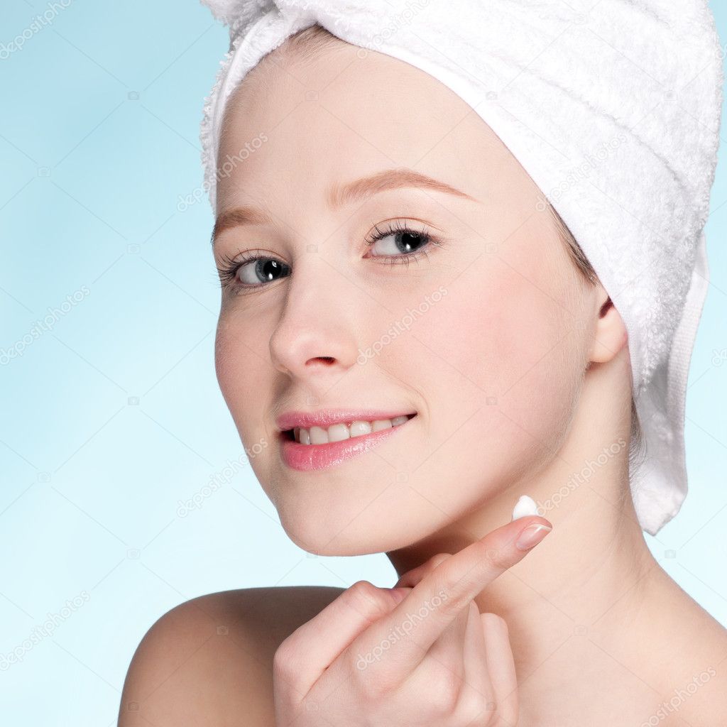 Beautiful woman applying moisturizer cream on face