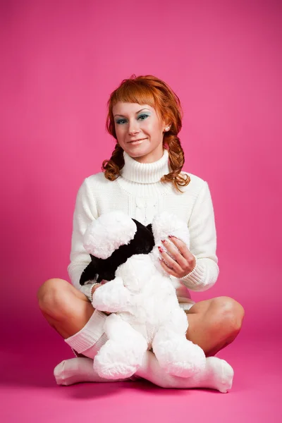 Πορτρέτο του τους μια κοκκινομάλλα κοπέλα σε έναν λευκό πουλόβερ με ένα μαλακό παιχνίδι — Φωτογραφία Αρχείου