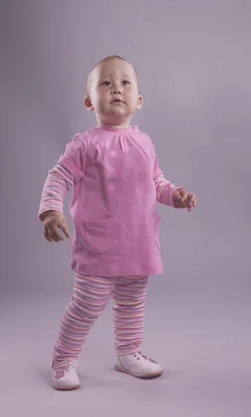 En liten flicka i rosa klänning poserar i studio — Stockfoto