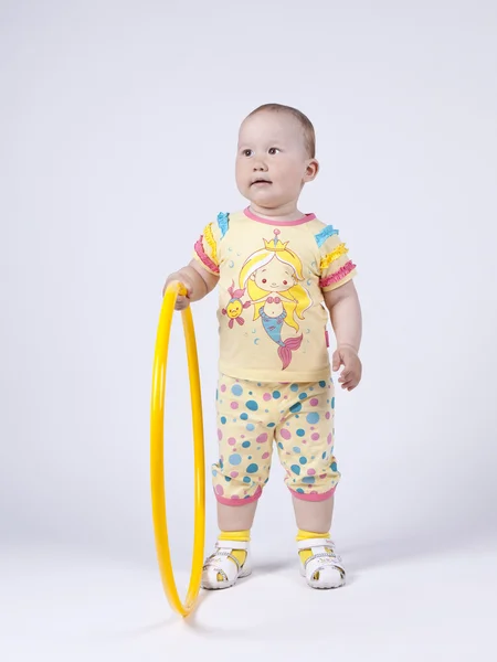 En liten flicka i en gul klänning som poserar i studio med en hula hoo — Stockfoto