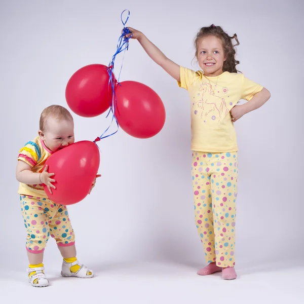 赤い風船で遊ぶピンクのパジャマで 2 つのかわいい女の子 — ストック写真