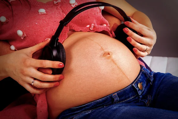 Barriga de mulher grávida com um ouvido musical — Fotografia de Stock