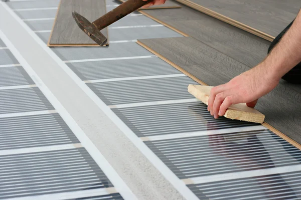 Homem instalando piso laminado sobre sistema de aquecimento de carbono infravermelho — Fotografia de Stock