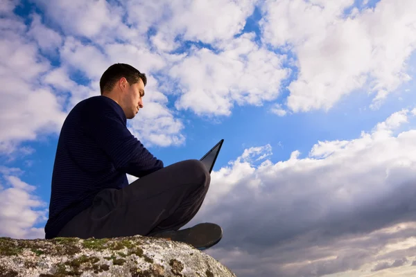 stock image Young man sitting on the top of mountain working with laptop