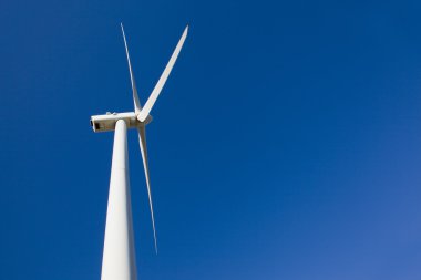 White wind turbine against blue sky clipart