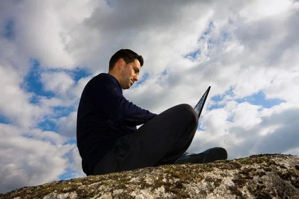 Young man sitting on the top of mountain working with laptop — Stock Photo, Image