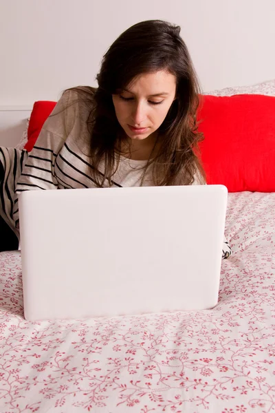 Giovane bella donna sdraiata sul letto con computer portatile — Foto Stock