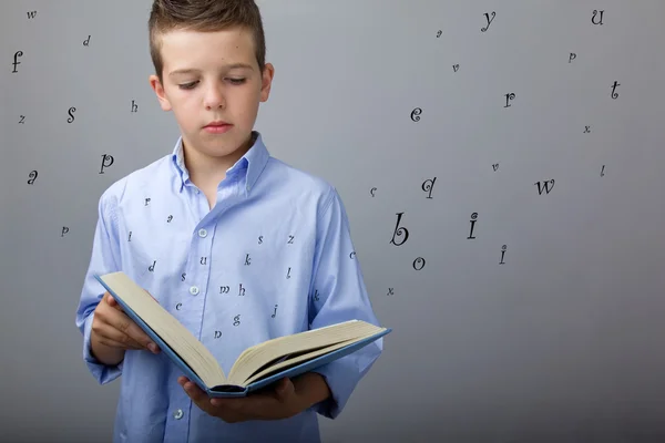 Söt pojke läser en bok med flygande bokstäver, studio skott — Stockfoto