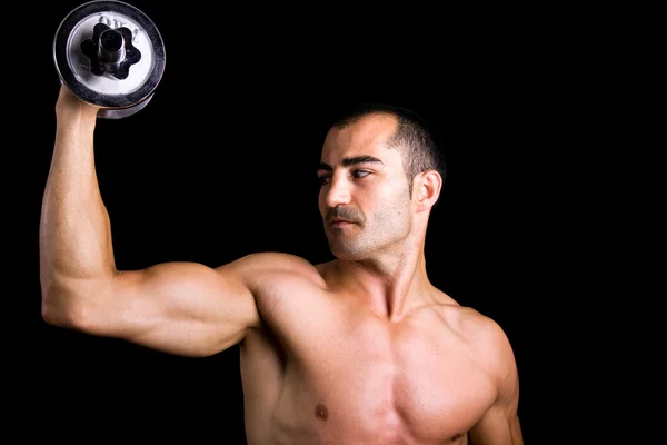 Muskulöser junger Mann hebt Hanteln auf schwarzem Hintergrund. — Stockfoto