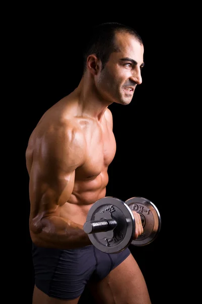 Musculoso joven levantando pesas sobre fondo negro . — Foto de Stock