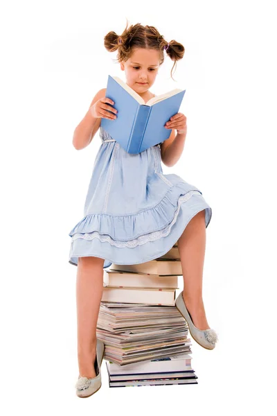 Imagen de colegiala sentada en el montón de libros y leyendo uno —  Fotos de Stock