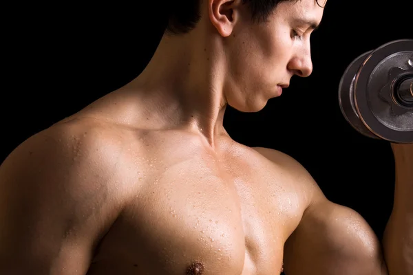 Primer plano del joven musculoso levantando pesas sobre fondo negro —  Fotos de Stock