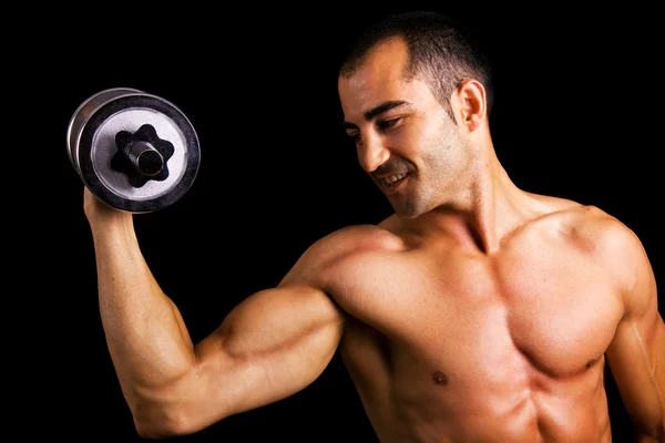 Junger muskulöser Mann hebt Hanteln vor schwarzem Hintergrund — Stockfoto