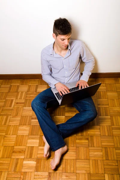 年轻男子坐在地上在红磡的便携式计算机上工作 — 图库照片