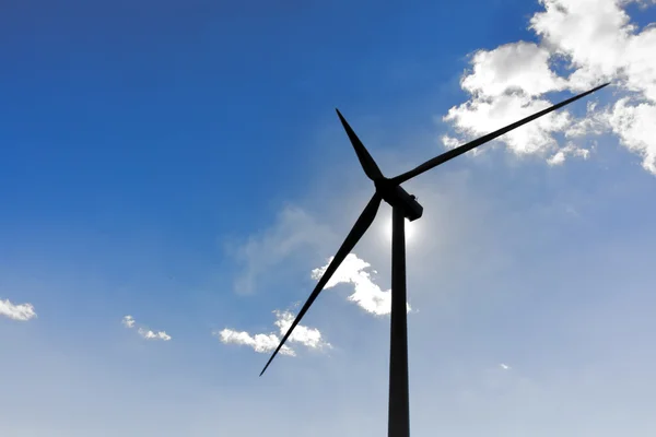 Turbina eolica nella luce posteriore del sole con cielo blu e clou — Foto Stock