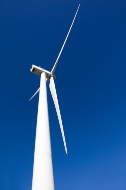 White wind turbine generating electricity on blue sky clipart